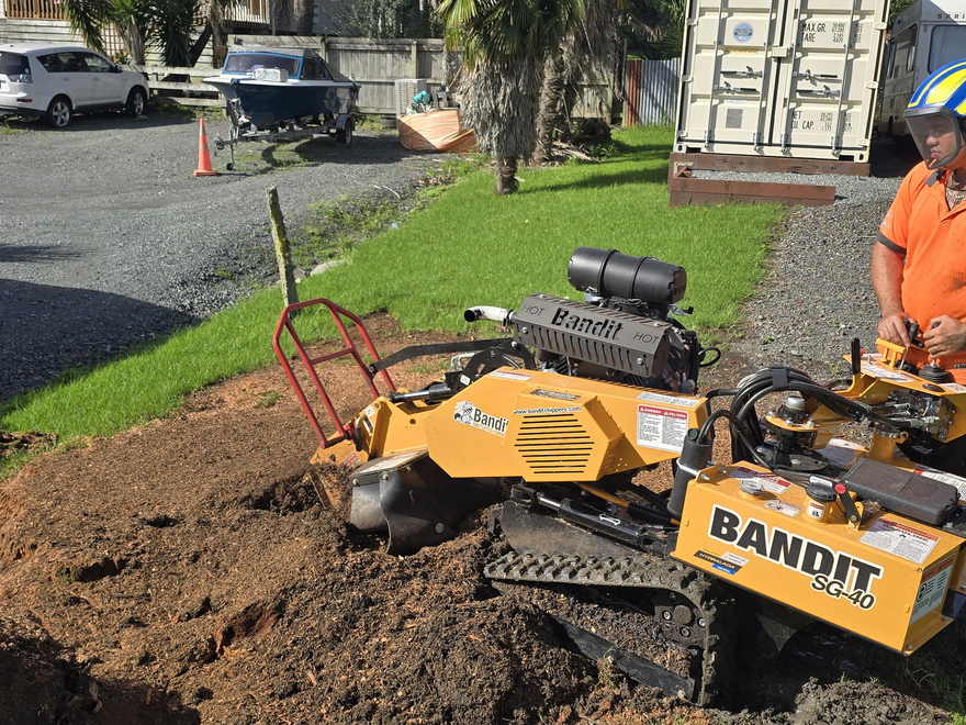 Tracked stump grinder chewing a large stump down into wood chips beside a gravel driveway